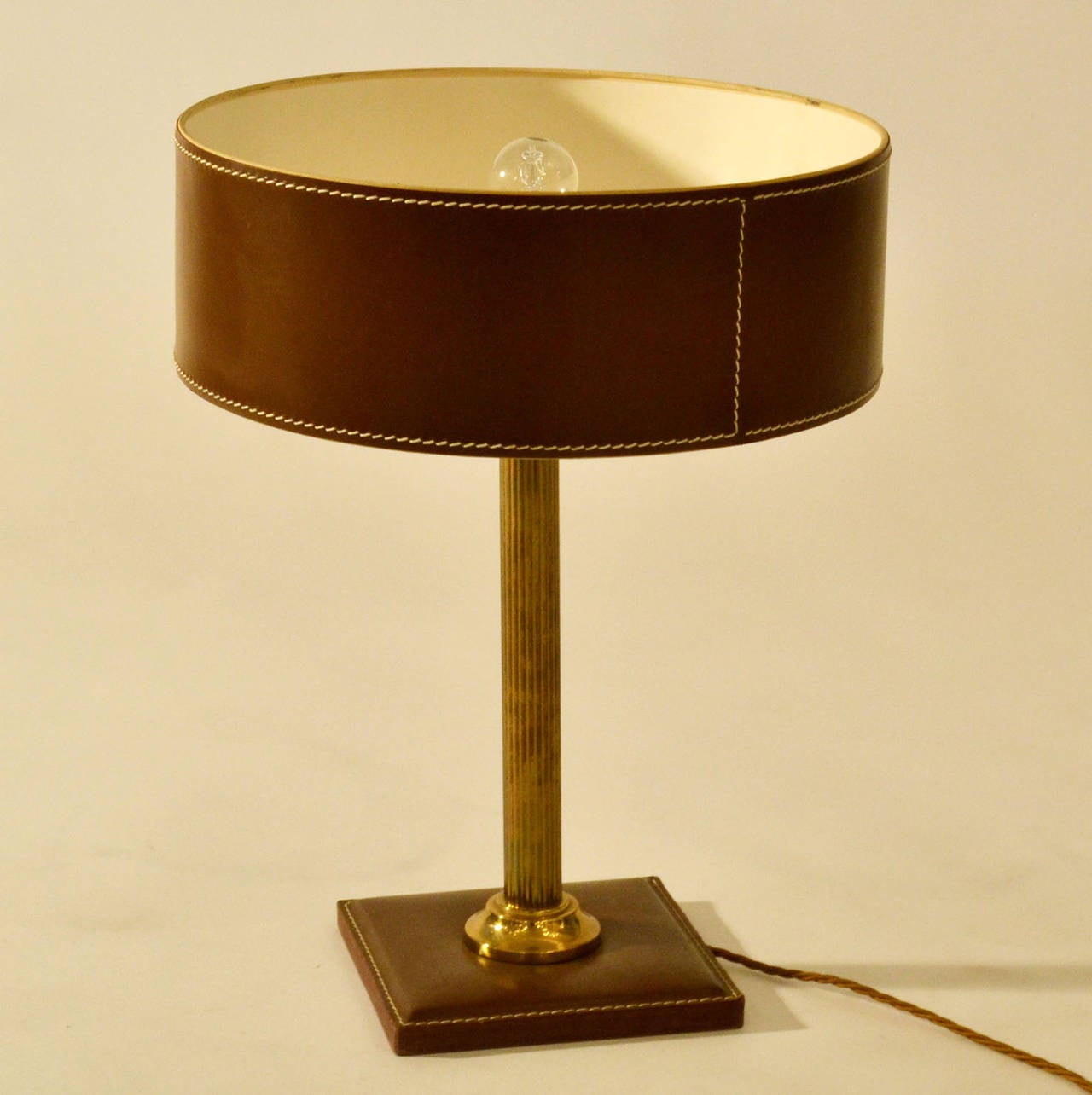 Hazel nut brown leather cladded table lamp with a round shade and square base with detailed contrasting stitching on a brass stem.