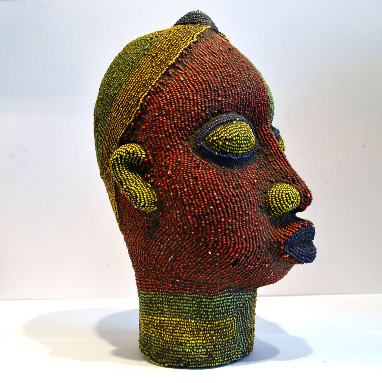 Brightly colored beaded terracotta head commissioned in the 1960s to decorate wealthy Nigerian homes. The terracotta sculpture is inlaid with strings of beads over its ceramic form.
The artist was influenced by 16th century Benin bronze.