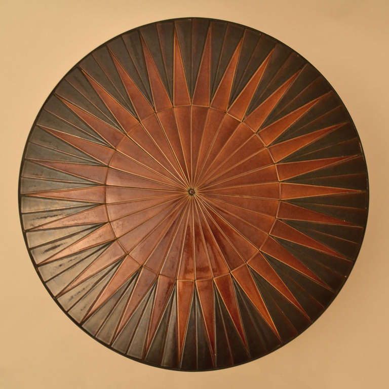 Burned orange and brown ceramic round coffee table tiled with triangular glazed segments into a sun or star array design on a black metal frame.