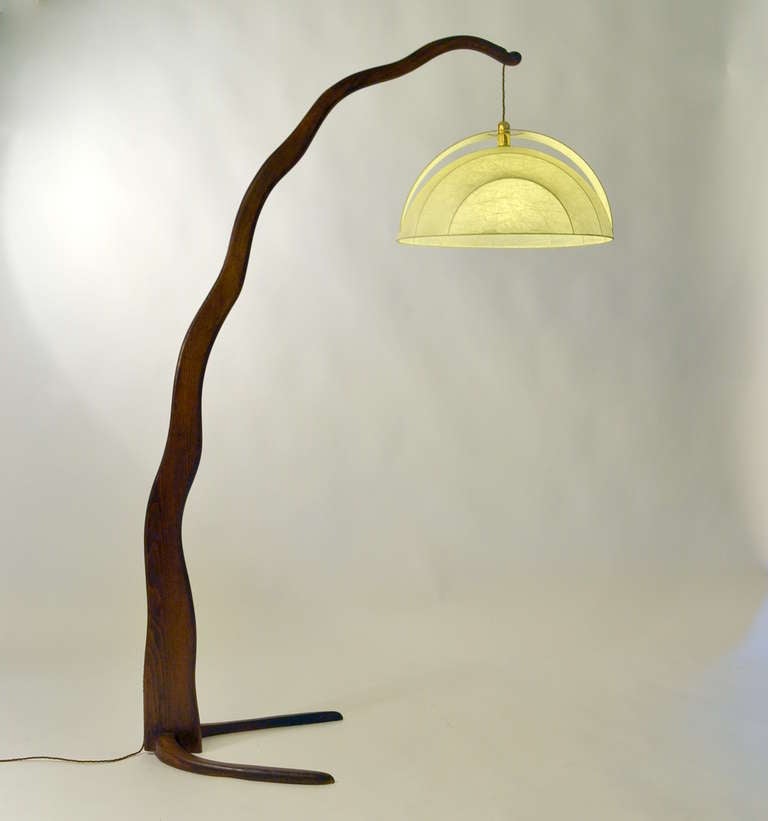 Organic hand carved wooden floor lamp with a unique sculptural shape. 
The electric wire is incorporated in the design, it lays in a groove along the arched stem. The hood is shaped like a flower and made of stretched fiber.