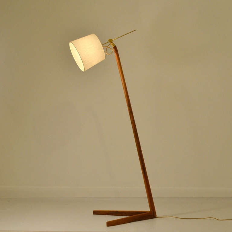 Floor lamp with adjustable light source and carved and V-shaped legs.