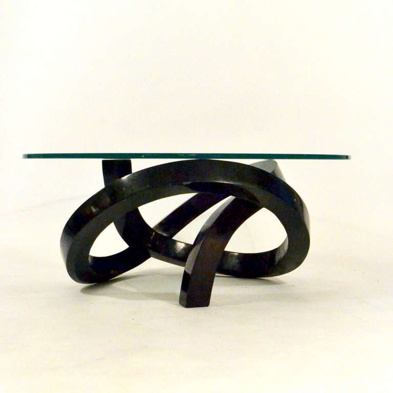 The coiled sculptural the coffee table is laminated in black marble. The glass rests on top of the organic formed base.