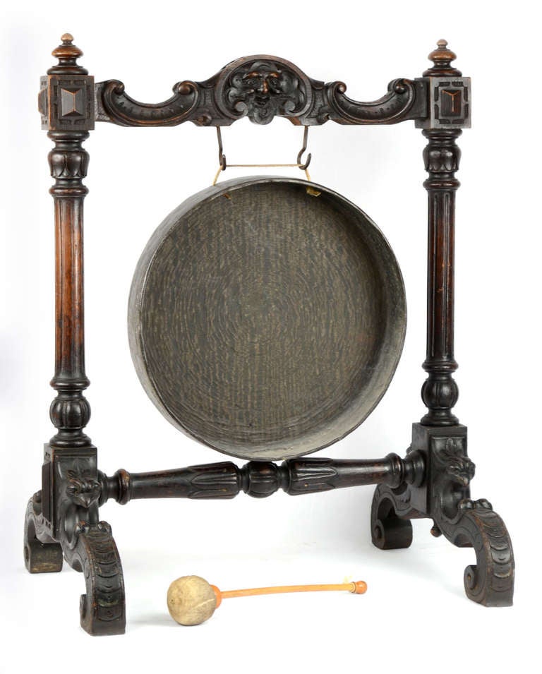 A nineteenth-century French gong suspended from a walnut stand supported by four carved c-scroll feet and topped with a low-relief sculpted mask.