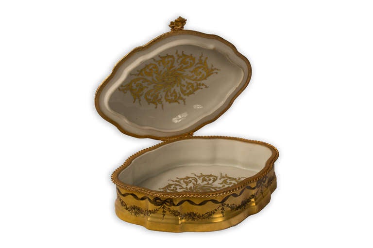 A beautiful, Louis -XV-style porcelain box with cover festooned with delicate paintings of ribbons, garlands, and a large central cartouche representing the Fine Arts on the exterior and cold-painted gold foliage on the interior.