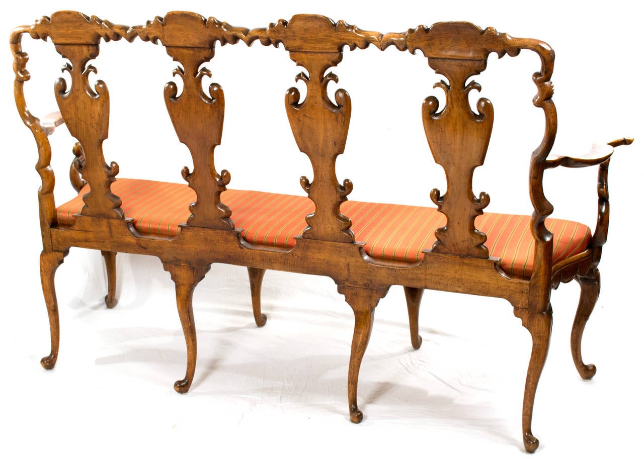 An sinuously carved walnut couch, carved in Venice during the third quarter of the nineteenth-century in the style of high Rococo. The back of the couch is formed by a series of four auricular back splats and stands on eight cabriole legs — the