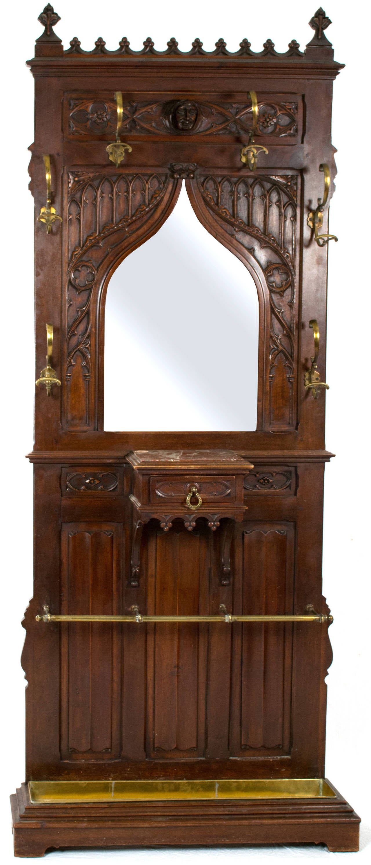 A very fine walnut hall tree with carved linen-fold paneling, ogee arches, trefoils, leaves, and — surmounting the bevelled mirror — a mask of the Green Man. The hall tree features six elaborate and beautiful brass s-shaped hooks, a brass bar and