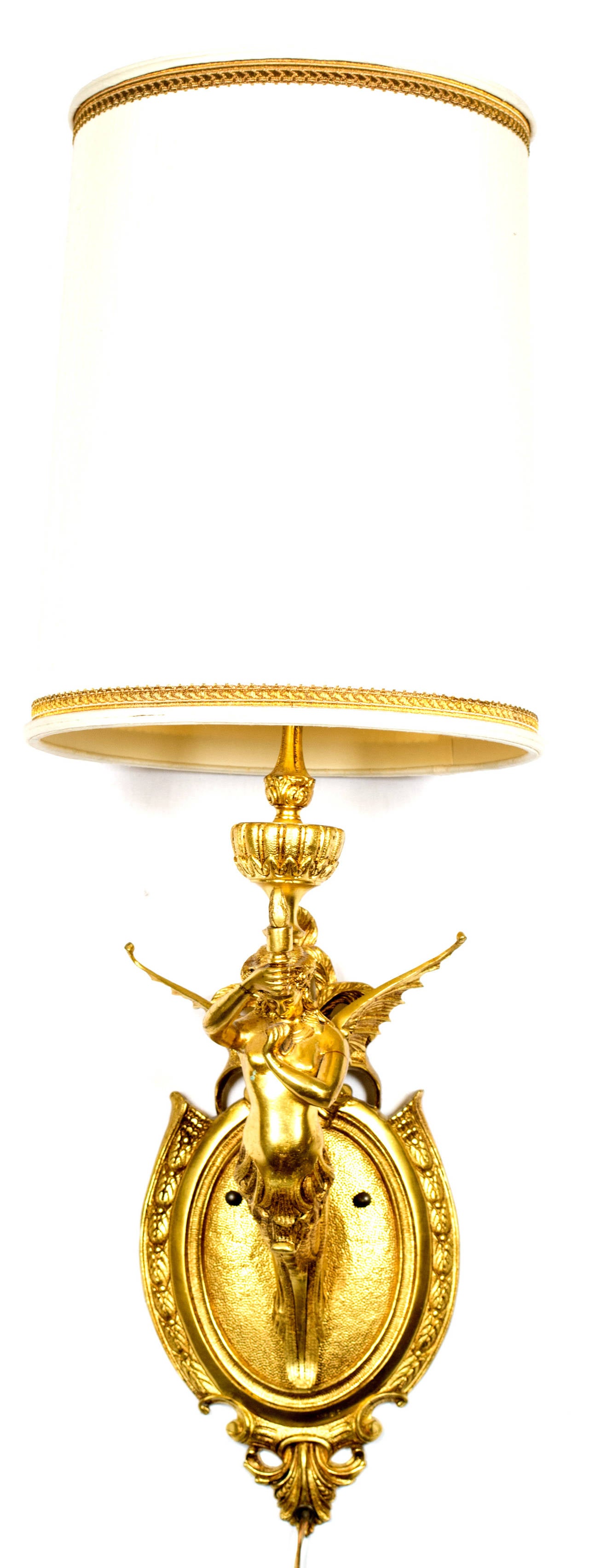 A gilt bronze wall sconce in the form of a sculpted mermaid with wing holding a torch with shade; made in France during the turn of the century.