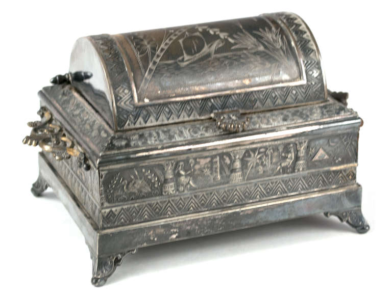 This American-made, Aesthetic-Movement jewelry box features a frieze of Egyptian courtiers and the nile.  The feet are upturned acroteria, with handles made of honeysuckles — motifs common to both Greek and Egyptian art. The work has three