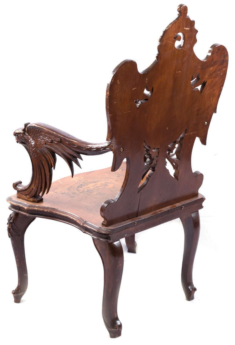 The back, arms, legs, and feet of this unusual chair feature full-relief carvings of eagles and wings. The back splat and seat are decorated with detailed marquetry Black Forest scenes of animals in dyed and hot-sanded fruitwoods.