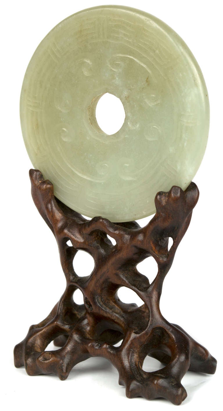 A pierced celadon colored jade disc, carved with cloud and thunder patterns. The disc surmounts an unusual wood stand, carved to resemble a sacred mountain.