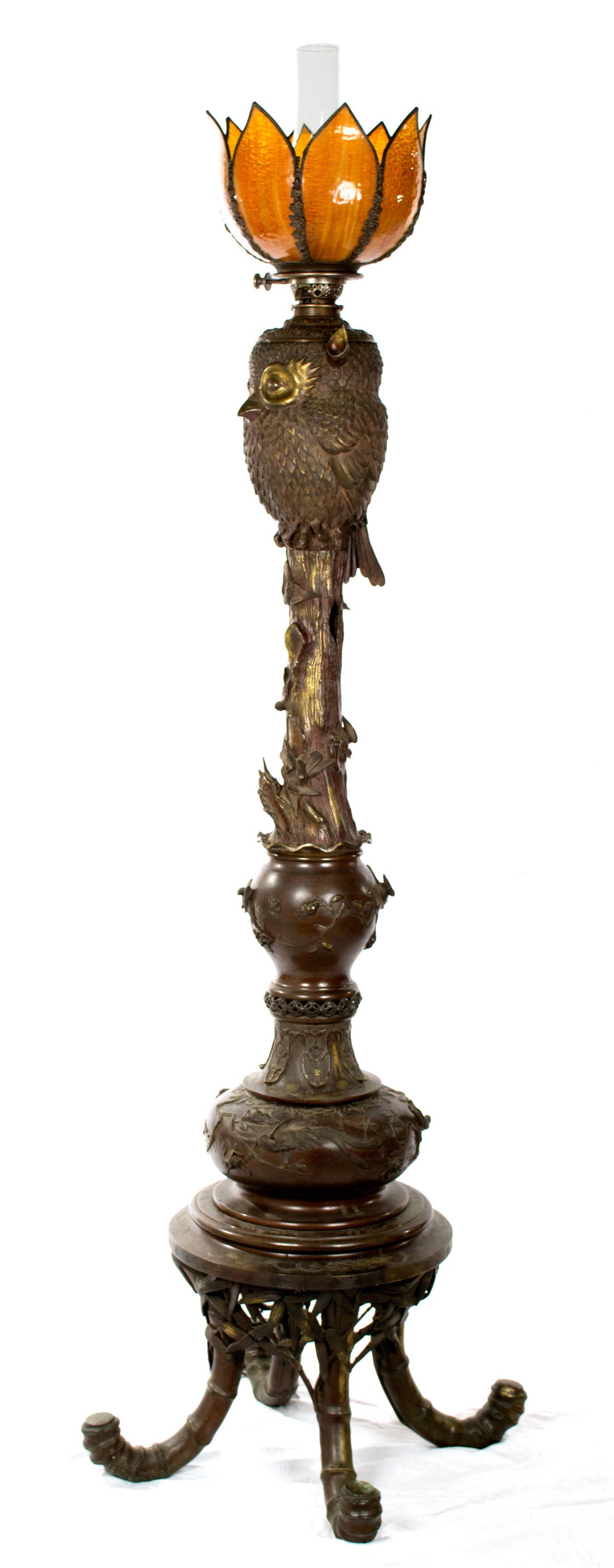 This large floor lamp was made in Japan during the first quarter of the 20th century, and features a large owl with sitting atop a column in the form of a tree truck festooned with vines and supported by four large cane feet. The lamp is surmounted