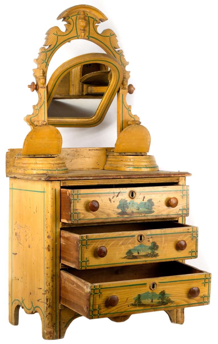 A buttermilk painted, children's pine dresser mirror inset in carved and painted surrounds and unusual compartments on the mirror base; three drawers, each centered with a landscape painting.