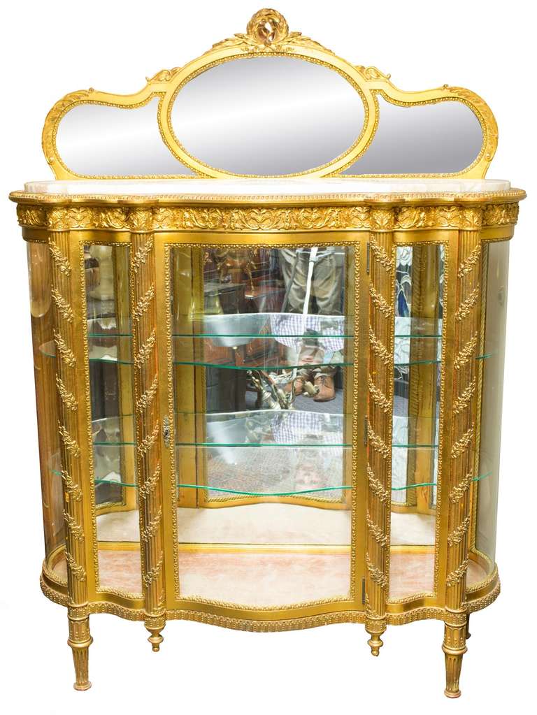 A large vitrine with glass shelves, gilt and carved wood case, interior mirrored back, and inset white marble top with segmented mirrored garniture with three, bevelled sections.