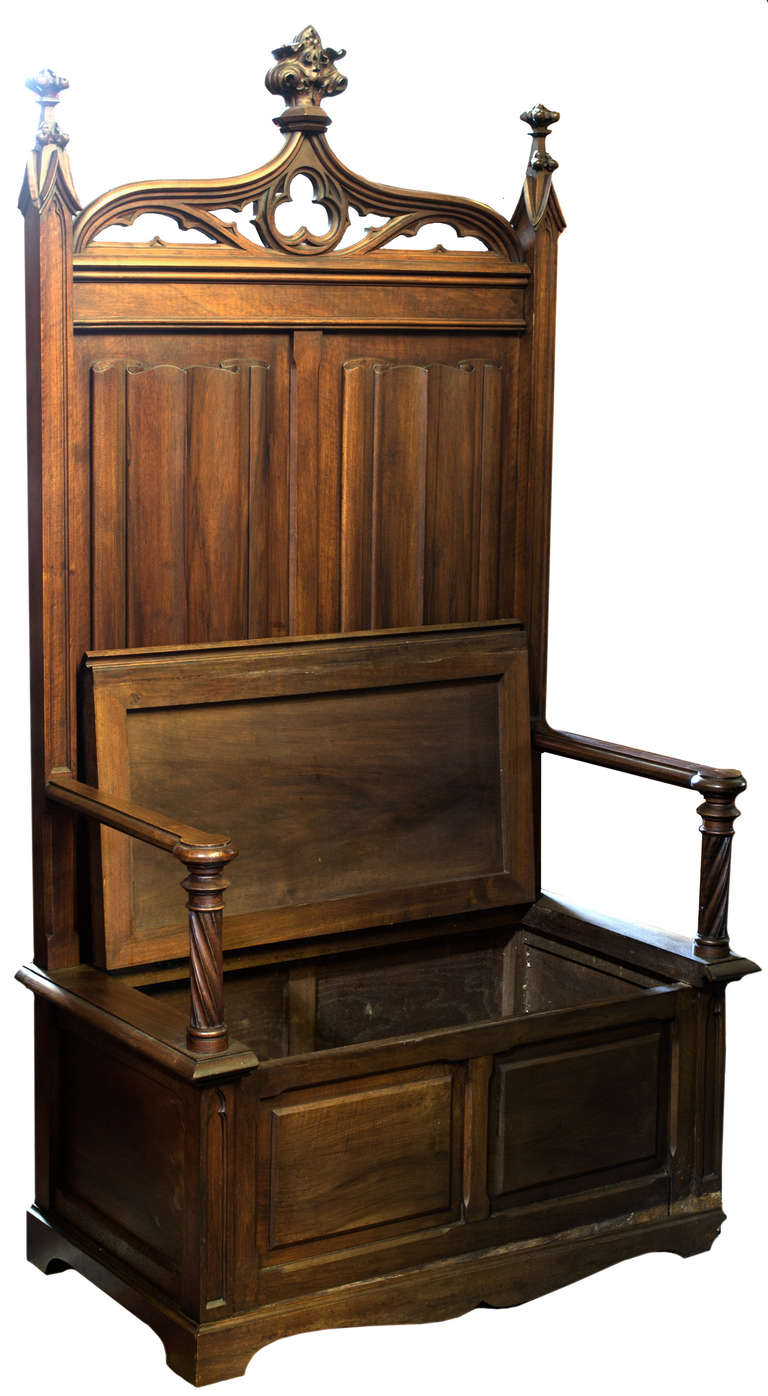 Also known as a box settle, this large bench with carved columnar arms and high back, featuring large carved linen-folds, and surmounted with an arched ogee arched pediment with a central trefoil, has a large seat which opens to reveal a storage