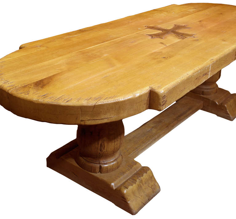 An unusually thick top refectory table with lobed ends and a carved Maltese or Latin cross in the center of the table. The legs are thick, carved bulasters and sit on a sturdy tressle-form base.