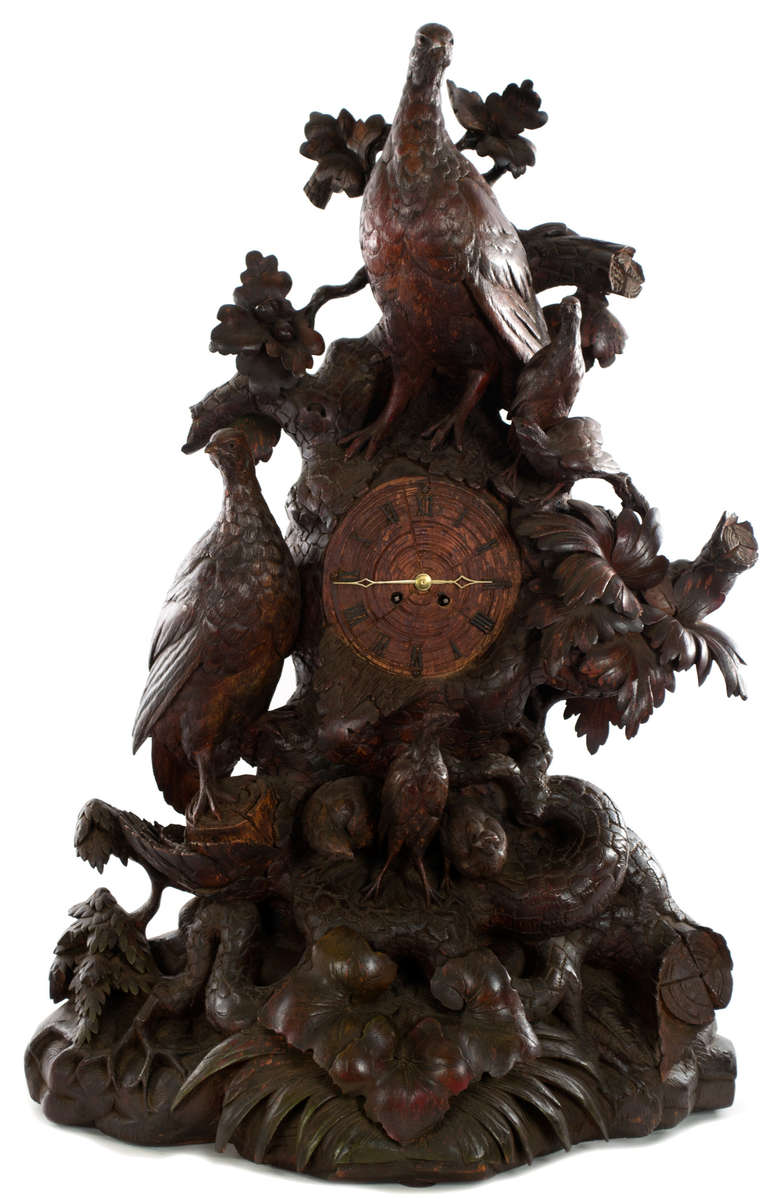 The body of the clock is a full-relief carving of a tree trunk — complete with roots, branches, leaves, and ground cover — in which a two large grouse and their clutch of chicks take shelter. On the base of the clock is a small painted marking of
