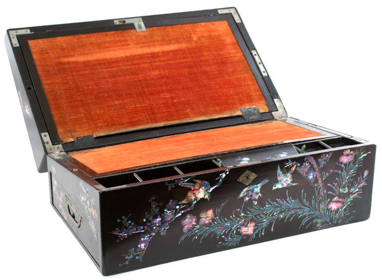 A particularly fine and luxurious Art Nouveau lap desk with cantered edges, the exterior in black lacquer and inlaid with extensive mother-of-pearl to create colorful birds and flora. The box opens to reveal a pink velvet writing surface and brass