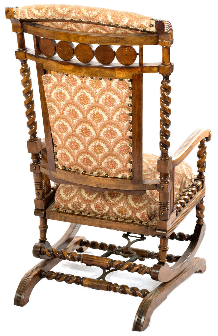 A rocking chair made by George Hunzinger featuring a variety of virtuosic carving and turning techniques; with petite-point diaper pattered seat and back in silk and bordered with brass studs.