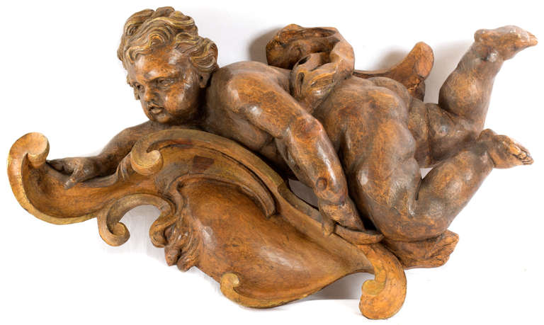 A fanciful, full-relief carving of a cherub (a.k.a. putto) recumbent on a large c-scroll, made in France during the last quarter of the 19th century.