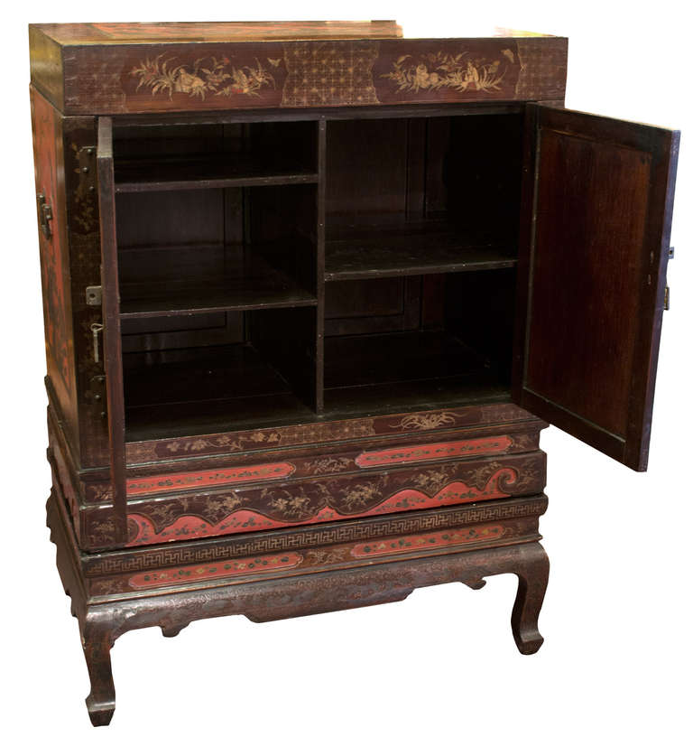 A large, red-lacquer Chinese cabinet, beautifully painted and gilt with multi-figural scenes of scholarly life, and with doors and drawers that open on each side of the piece, suggesting that the cabinet is meant to be in the center of a room. The