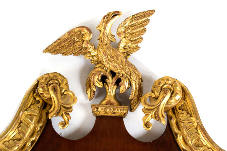 A large, mirror featuring carved gilded edges and topped with a broken pediment centered with a large eagle with spread wings in the style of William Linnell.