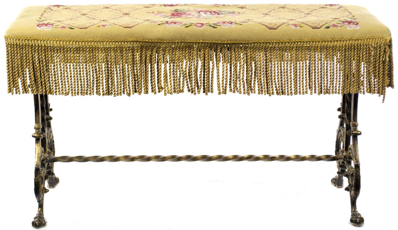 Standing on four lion paws decorated with elaborate C scrolls and acanthus leaves, with hand-twisted wrought iron braces and bars, the seat of this bench features beautiful rose garlands in petite and gros-point needlework edged with golden tassels.