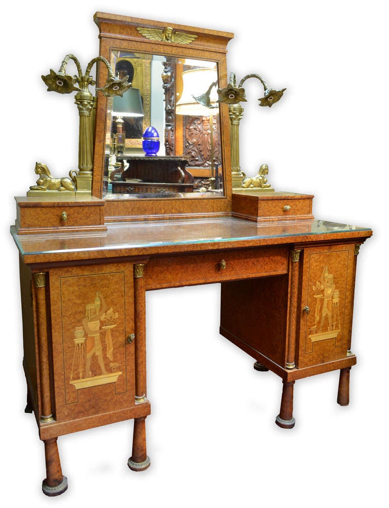 A fanciful French vanity made of satinwood and inlaid in exotic and fruit woods. The bevelled mirror is topped with a gilt bronze figure a winged woman and on either side are elaborate gilt bronze lamps — each with two working light — atop sphinxes.