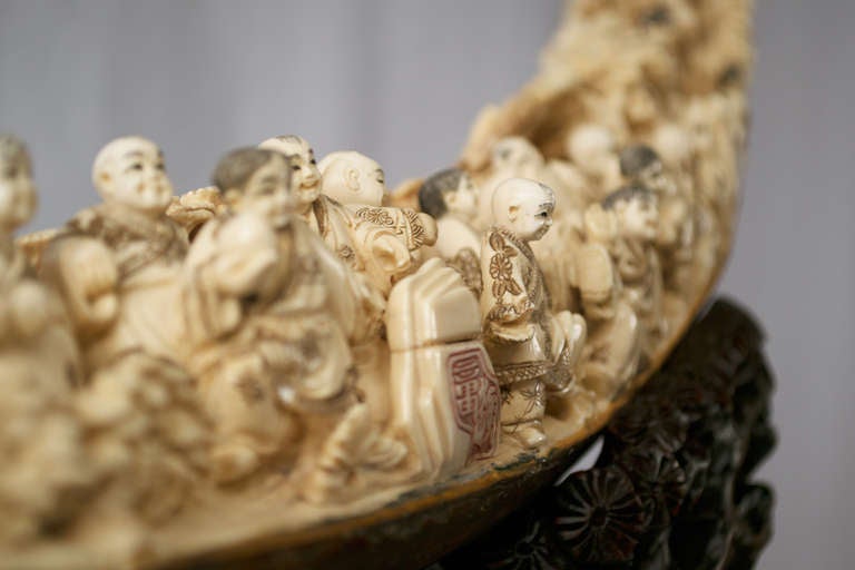 A large pre-historic mammoth tusk taken from the Siberian permafrost, which has been carved with dozens of figures feeding a Buddha, by contemporary master sculptors in China and mounted on a custom-made, pierced stand in exotic wood.