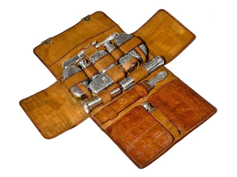 In genuine crocodile skin case with the initials C.H. discretely imprinted on the front.  Antique sterling silver pieces inside include hairbrushes, hip flask, manicure set, soap dish, clothes brush, shoe horn, penknife, assortment of bottles and