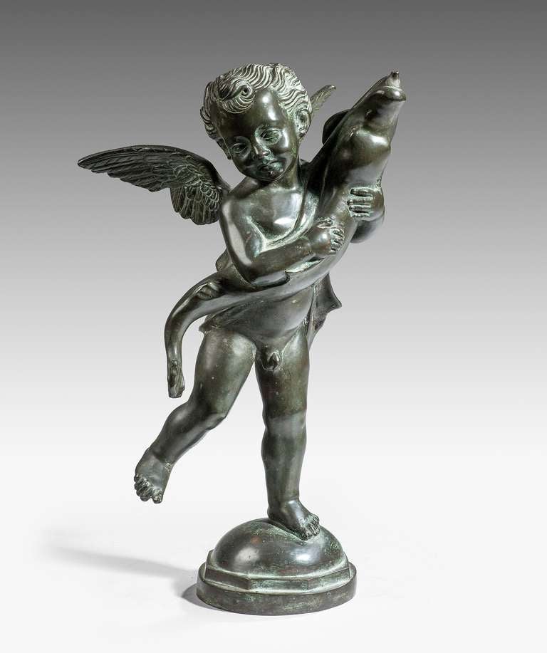 A late 19th century bronze fountain head in the form of a winged cherub holding a fish whose mouth is the spout of the fountain.