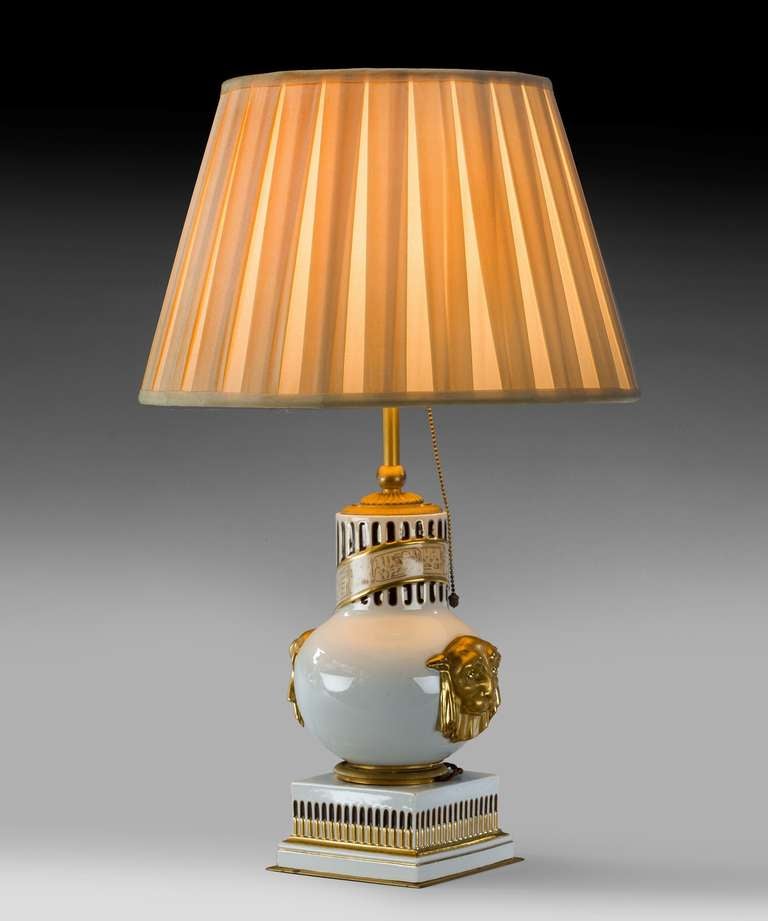 A French porcelain table lamp; designed in the Egyptian taste, decorated with fluting and a hieroglyphic scroll; having gilded panther heads to either side.