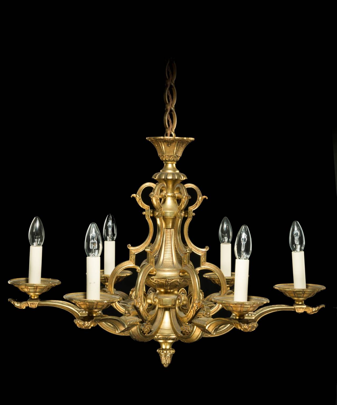 A Louis XIV revival chased brass six-light chandelier; the ring suspension above a central urn stem supported by scrolling strapwork decorated with acanthus leaves from which the chandelier's scrolling candle arms issue and terminate in dished drip