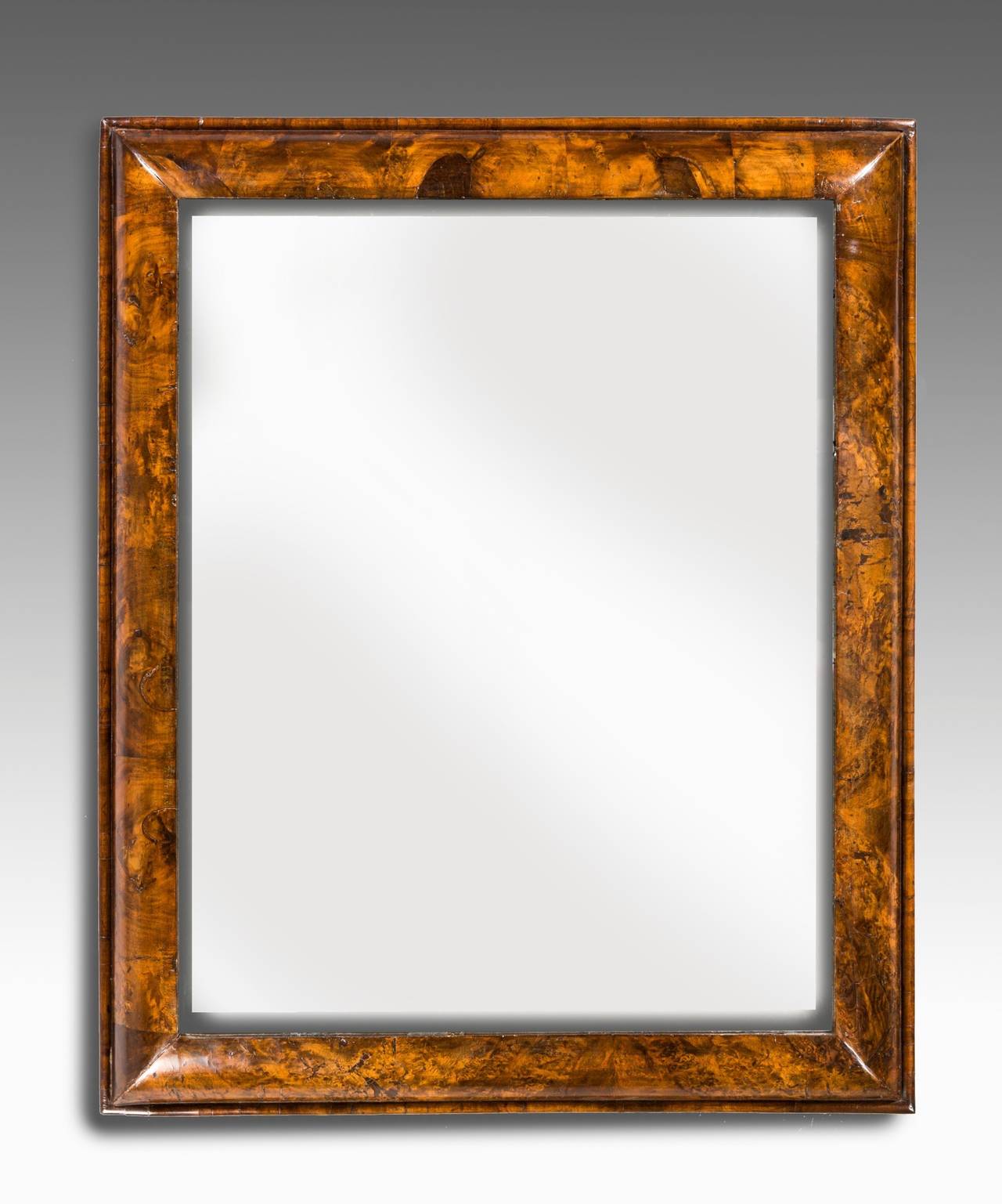 A Queen Anne period walnut veneered cushion mirror; retaining its original bevelled mirror plate.