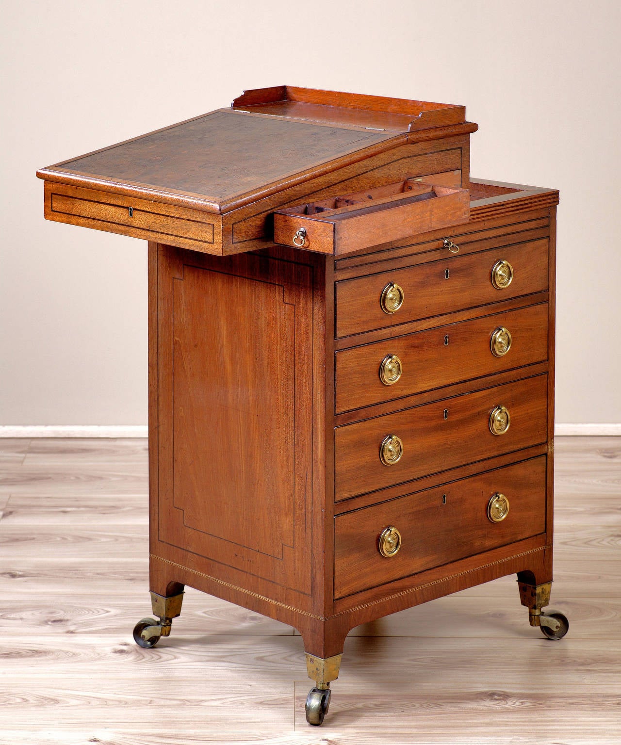 A George III Sheraton period mahogany davenport; having a pull-out pen wrest above drawers to the right hand side which are strung in ebony; the leathered writing slope opens to reveal an interior veneered in bird's eye maple. 

For more