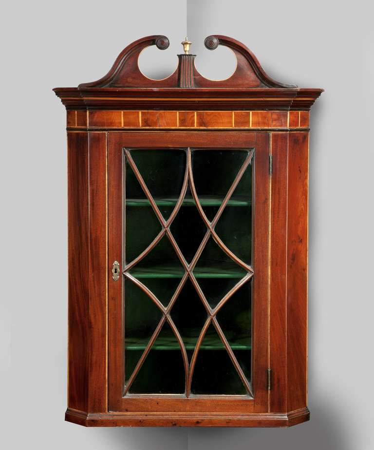 A George III Sheraton period mahogany hanging corner cupboard; the swan neck pediment above a boxwood strung cornice; the glazed door with an elegant astragal.