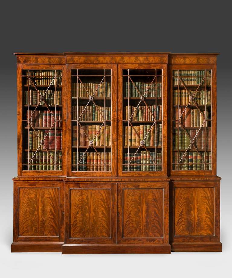 A fine Regency period mahogany breakfront bookcase; the cornice veneered in flame mahogany above astragal glazed doors which open to reveal adjustable shelves to the centre and fixed shelves to the wings, below are panelled cupboard doors veneered