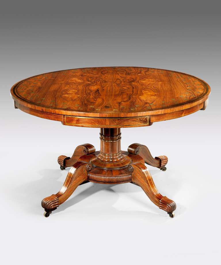 A Regency period rosewood and brass inlaid centre table; the well figured top double strung in brass and inlaid with trailing ivy executed in brass above later frieze drawers; raised on a cluster column stem which terminates in a circular reeded