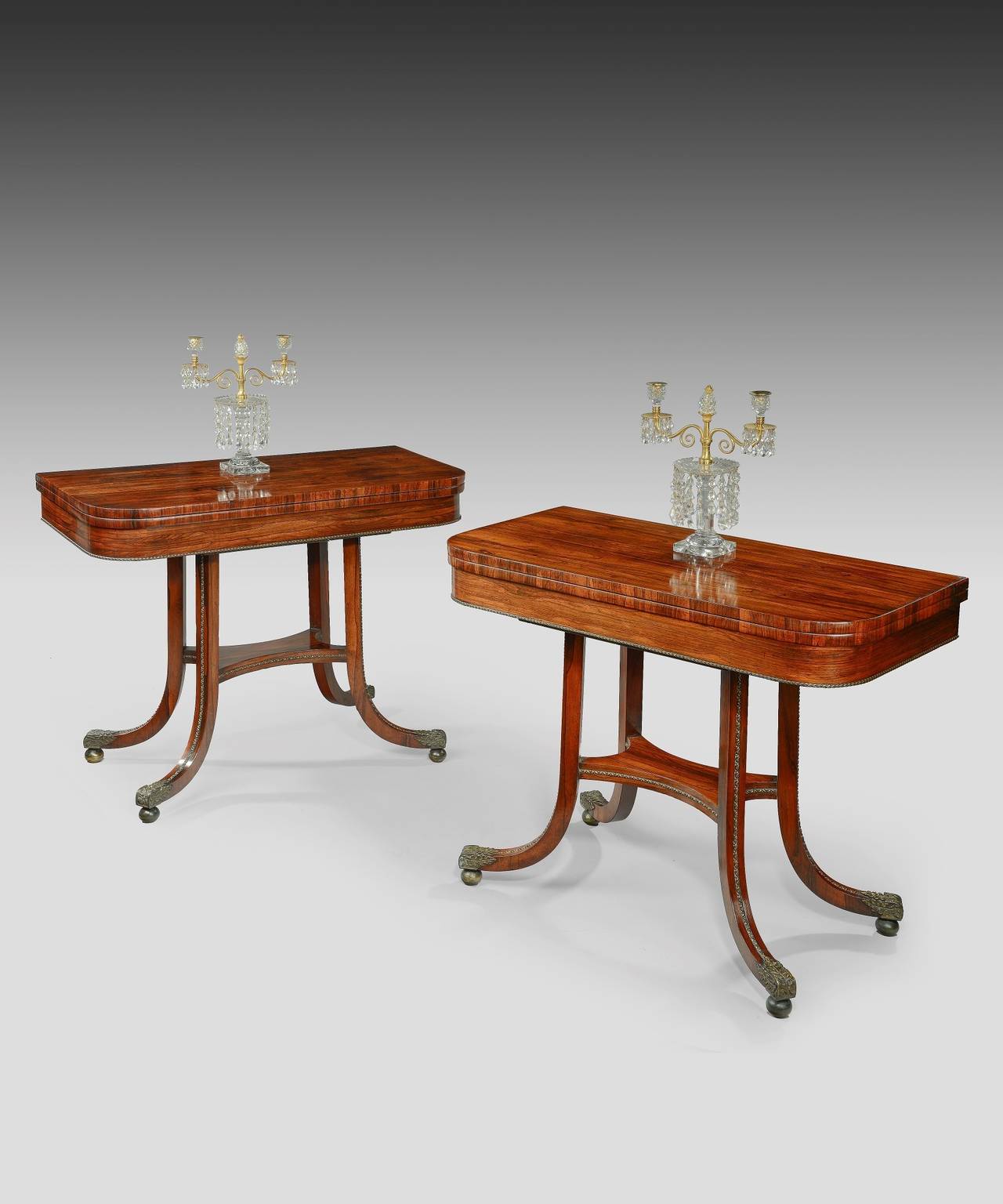 A handsome pair of Regency period rosewood veneered card tables; the well figured tops rotate and open to reveal a baize covered playing surface, raised on hockey stick legs which are decorated with ormolu and terminate in unusual oak leaf castors