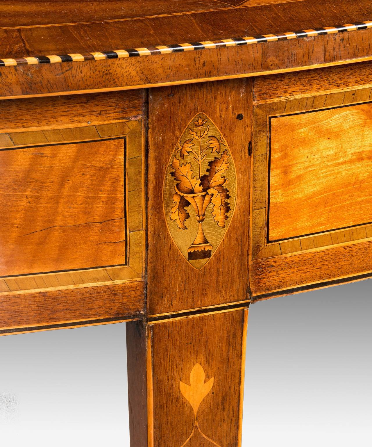 An Irish George III Sheraton period satinwood and sycamore veneered semi elliptical console table in the manner of William Moore of Dublin; the semi elliptical top with a central inlaid fan motif in boxwood on a sycamore ground from which extends