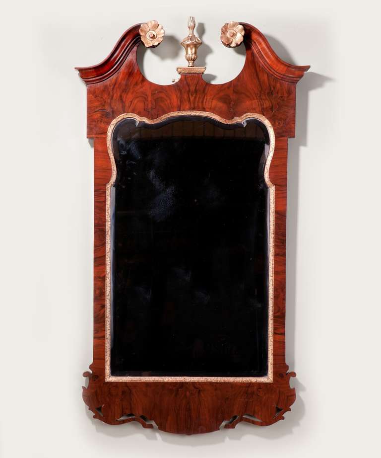 A George II walnut and parcel gilt mirror, the frame with a cross grain moulded swan neck pediment centered by a carved urn with later bevelled mirror plate.