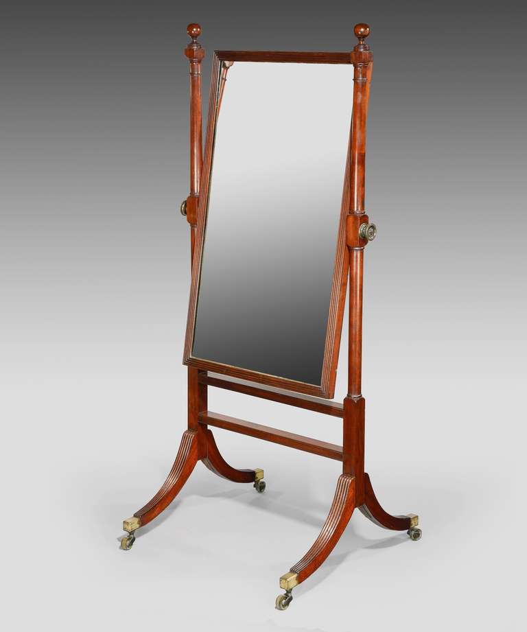 A Regency mahogany cheval mirrror; the original mirror plate set within a reeded mahogany frame and supported on turned and reeded end-supports which are topped by turned finials.