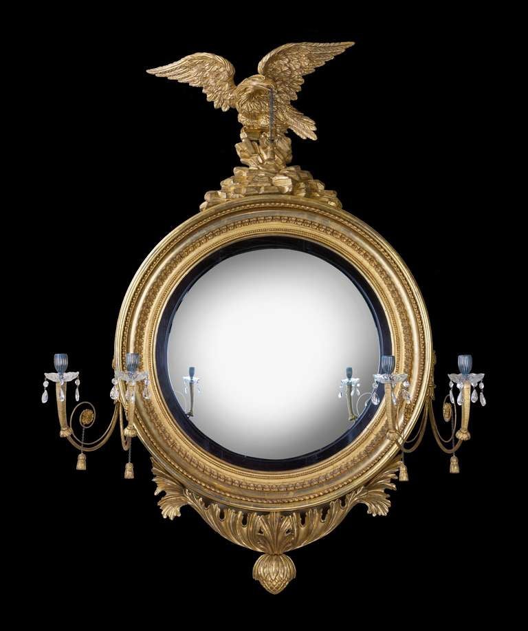 A large Regency period carved giltwood convex mirror; the convex mirror plate set within an ebonized slip and a crisply carved giltwood frame decorated with running acanthus leaves and a bead moulding surmounted by an eagle atop a rocky outcrop and