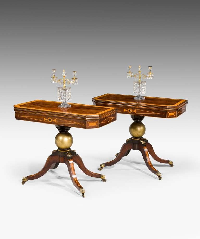 A fine pair of Regency period card tables veneered in rosewood; the card table's well figured top with amboyna crossbanding and canted corners opening to reveal a baize lined playing surface above a frieze geometrically inlaid with amboyna and a