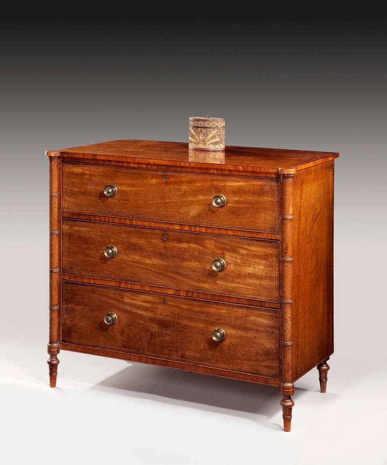A George III Sheraton period faded mahogany chest of drawers; the chest's well figured eared top cross banded in satinwood above three graduated drawers which retain their original brass knob handles, raised on ring turned feet. Strung throughout in