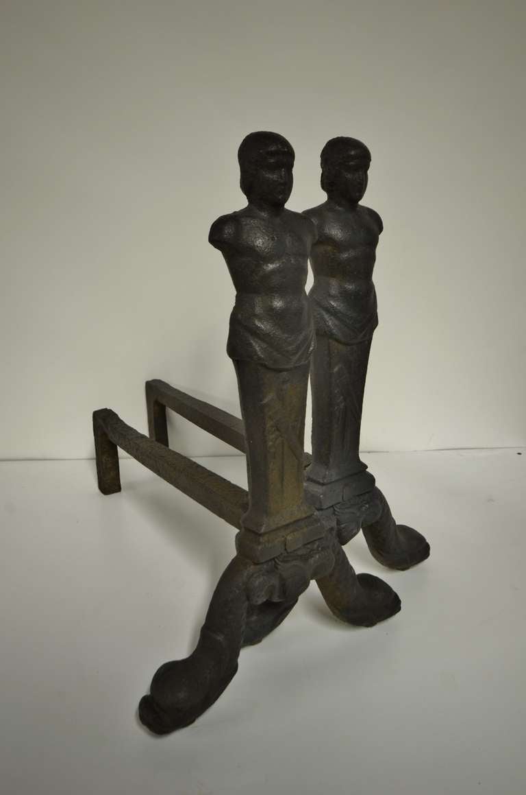 A rare pair of solid casted early 19th century (probably earlier) figurative andirons.
Displaying two armless, muscular male figures: Cretan Kouros; on the tapering arrow and quiver trophied plinths.
The men are standing on sea serpents.