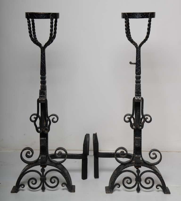 A tall and elegant pair of wrought iron fire dogs, with large wine bottle holders, rope twist handles and scrolling floral supporting feet.
