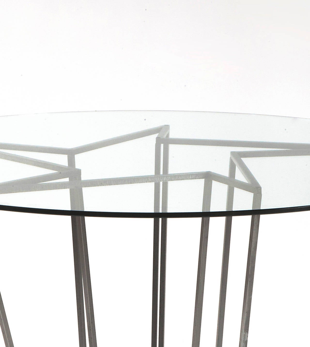 Table with a circular clear glass surface resting on a sculptural star-shaped steel structure.