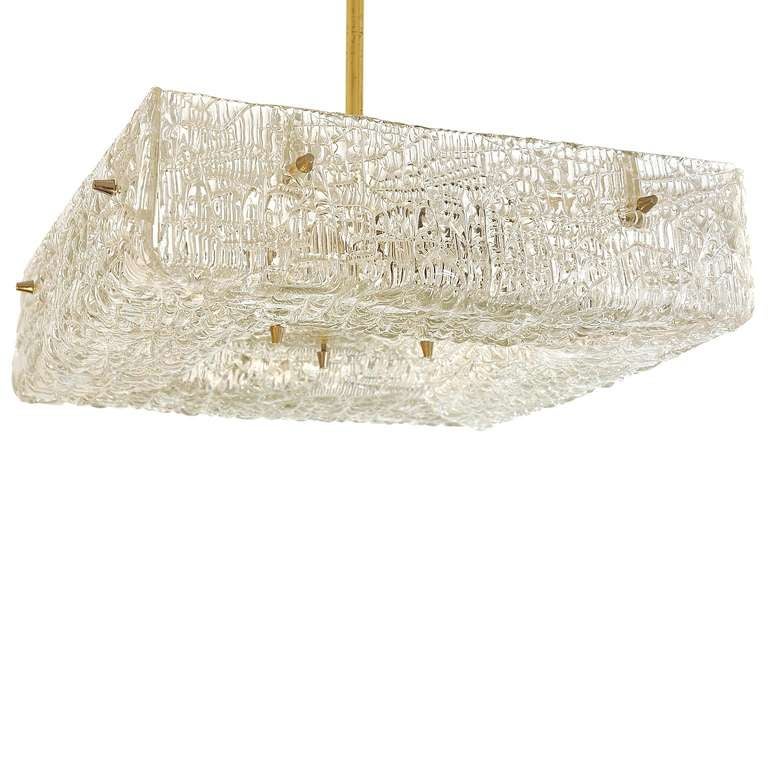 This Viennese Chandelier was designed and manufactured by J.T.Kalmar in 1950-60s. The pressed and cast glass takes form of a square and has an uneven surface. It has 12 small brass caps and 4 bulb sockets.
