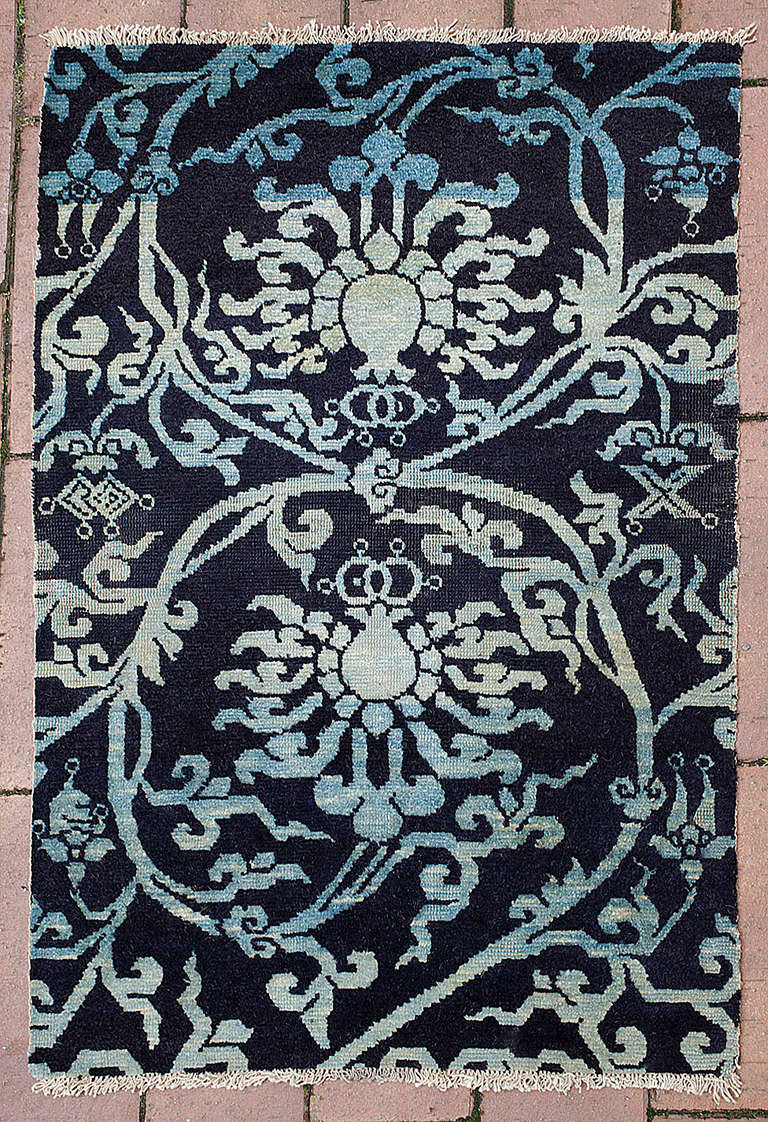 A charming Tibetan sitting rug (Shugden) dyed only with indigo of varying intensity. 

Two delicately drawn lotus flowers amongst scrolling foliage in light shades of blues sit against a dark blue background creating a simple yet elegant design.