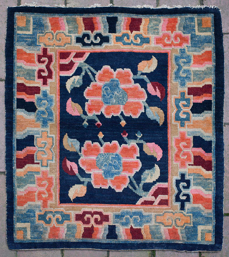 
This colorful Tibetan sitting rug, placed on top of a saddle, is full of joy and energy.

Two blossoming lotus flowers grow from behind rocks in opposing corners into the central field. The flowers are drawn with beautiful detail and skilfully